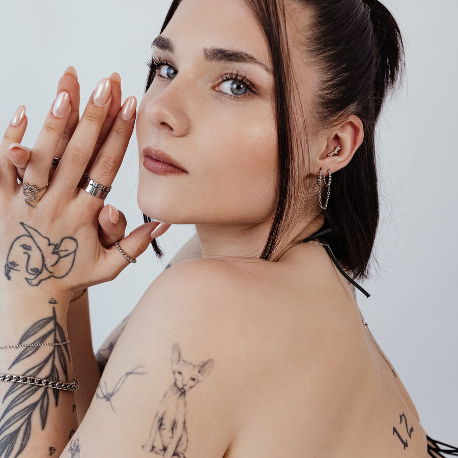 Donna con braccia tatuate indossa anelli piercing neri e argento nell'orecchio, profilo laterale