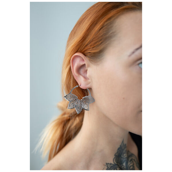 Pendientes plateados en forma de hoja en la oreja de una persona con cabello rojo