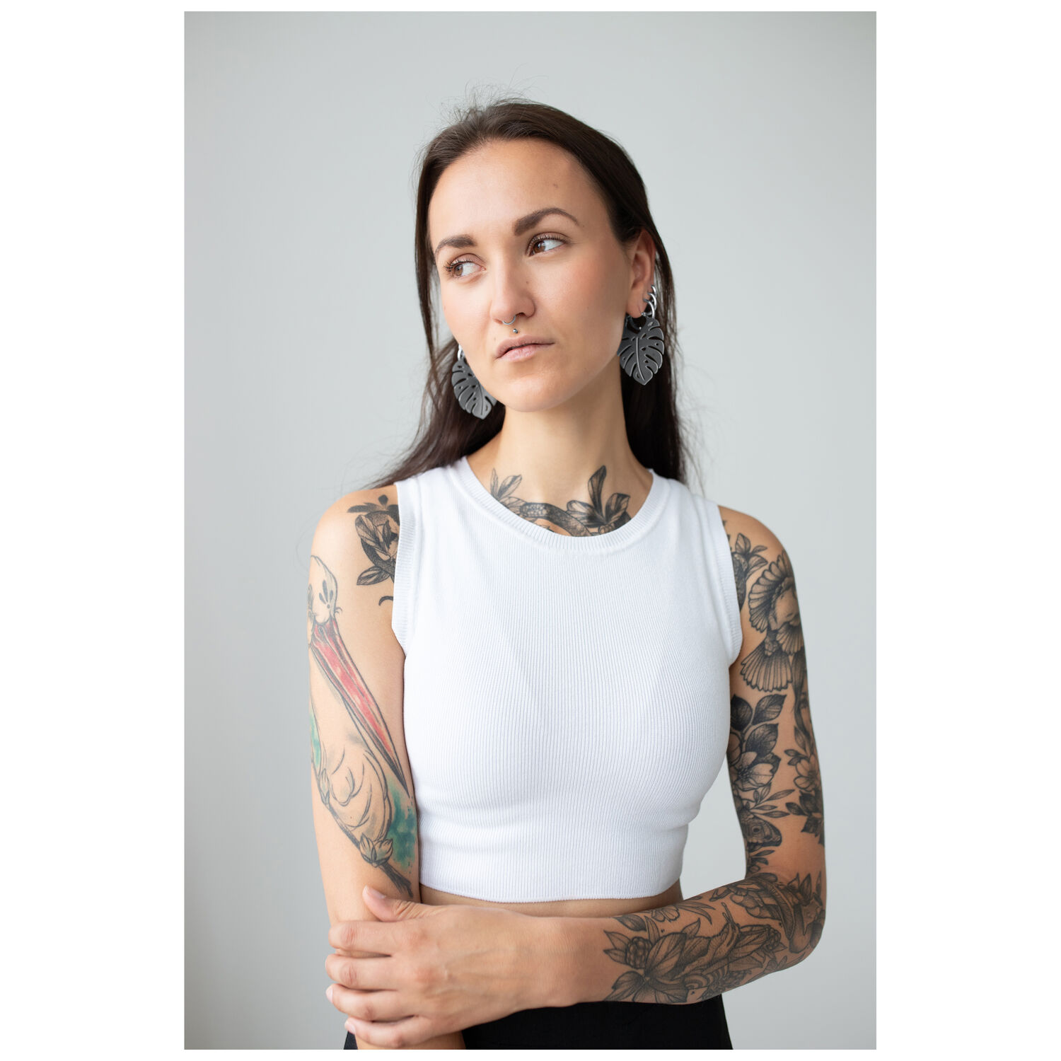 Monstera Leaf Hoops mit Frau im Studio Frau mit tätowierten Armen trägt Monstera Leaf Hoops Ohrringe, weißes Top