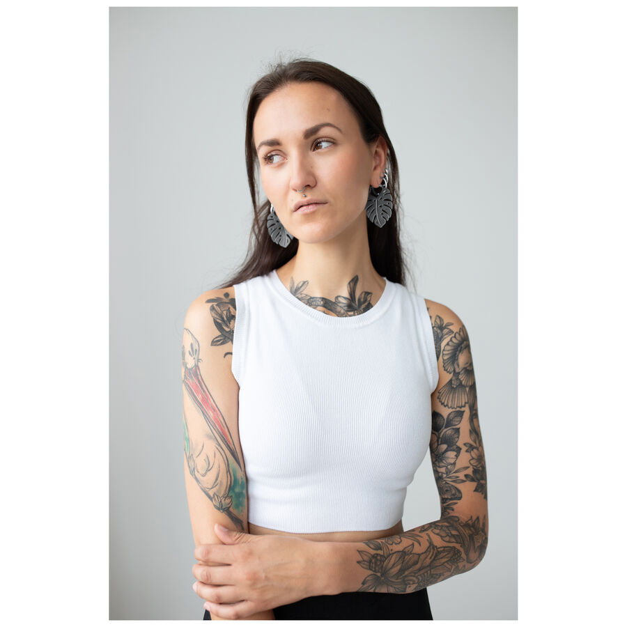 Nainen, jolla on tatuoidut käsivarret, käyttää Monstera Leaf Hoops -korvakoruja, valkoinen toppi