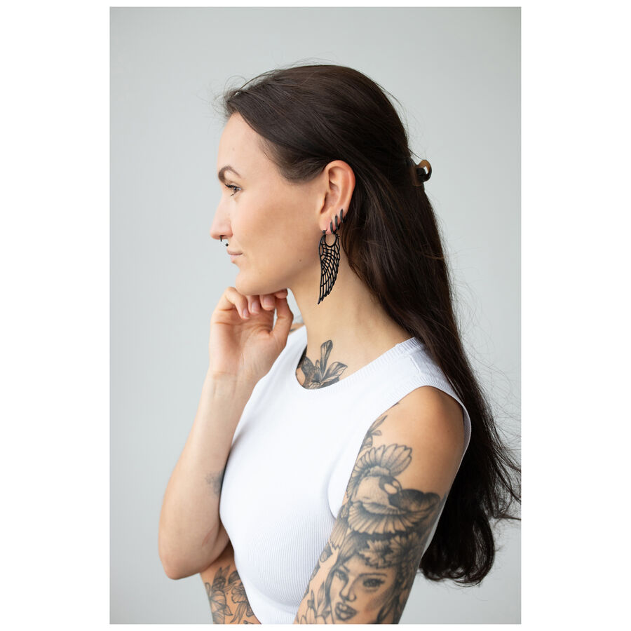 Donna con lunghi capelli scuri, indossa orecchini Wing Hoops neri e una maglietta bianca