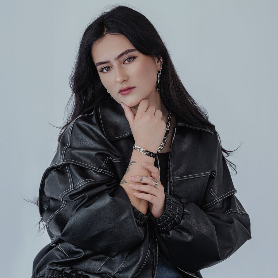 Donna con giacca di pelle nera indossa anello a catena in argento e bracciale abbinato su sfondo grigio