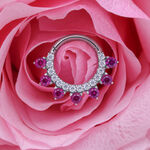 Anillo de piercing plateado con cristales rojos sobre pétalo de rosa rosa