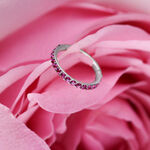 Anillo clicker plateado con cristales rojos sobre pétalos rosados