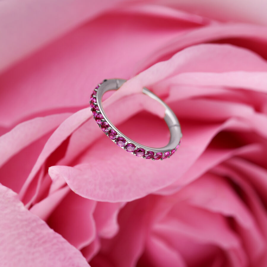 Anillo clicker plateado con cristales rojos sobre pétalos rosados