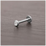 Accesorio de piercing de titanio plateado con cristal claro sobre superficie de madera oscura