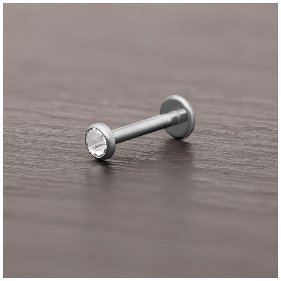 Accesorio de piercing de titanio plateado con cristal claro sobre superficie de madera oscura