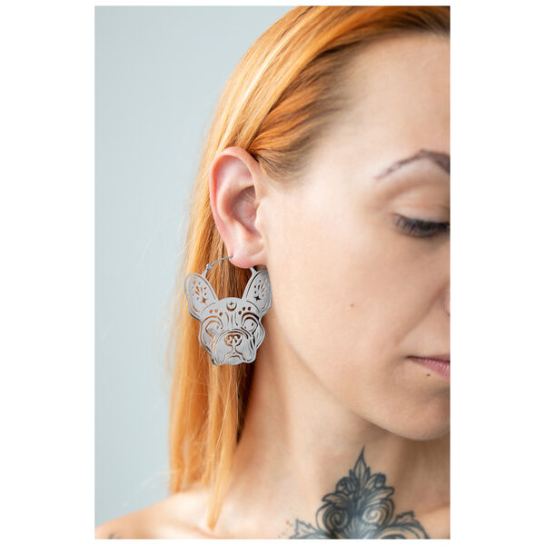 Aros de bulldog plateados en la oreja de una mujer con cabello claro y tatuaje