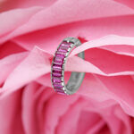 Anillo de piercing plateado con cristales baguette rojos sobre fondo de flores rosas