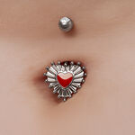 Piercing de ombligo con diseño de corazón rojo y acentos plateados sobre piel