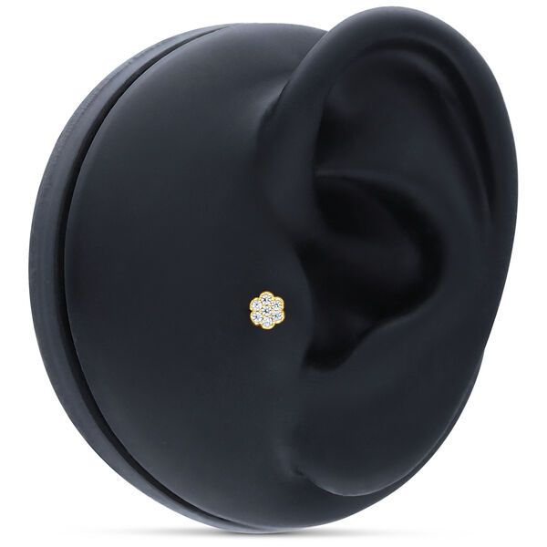 Accesorio dorado en forma de flor con cristales claros sobre modelo de oreja negro
