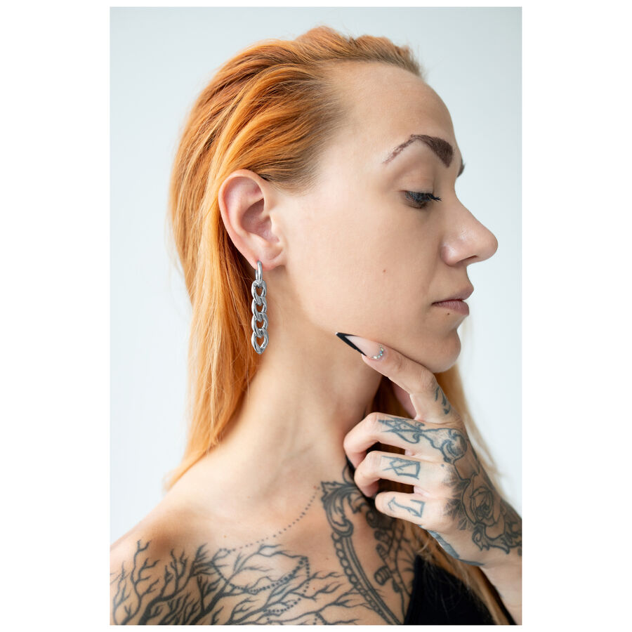 Aros plateados con diseño de cadena llevados en una oreja con mano tatuada y cabello rojo