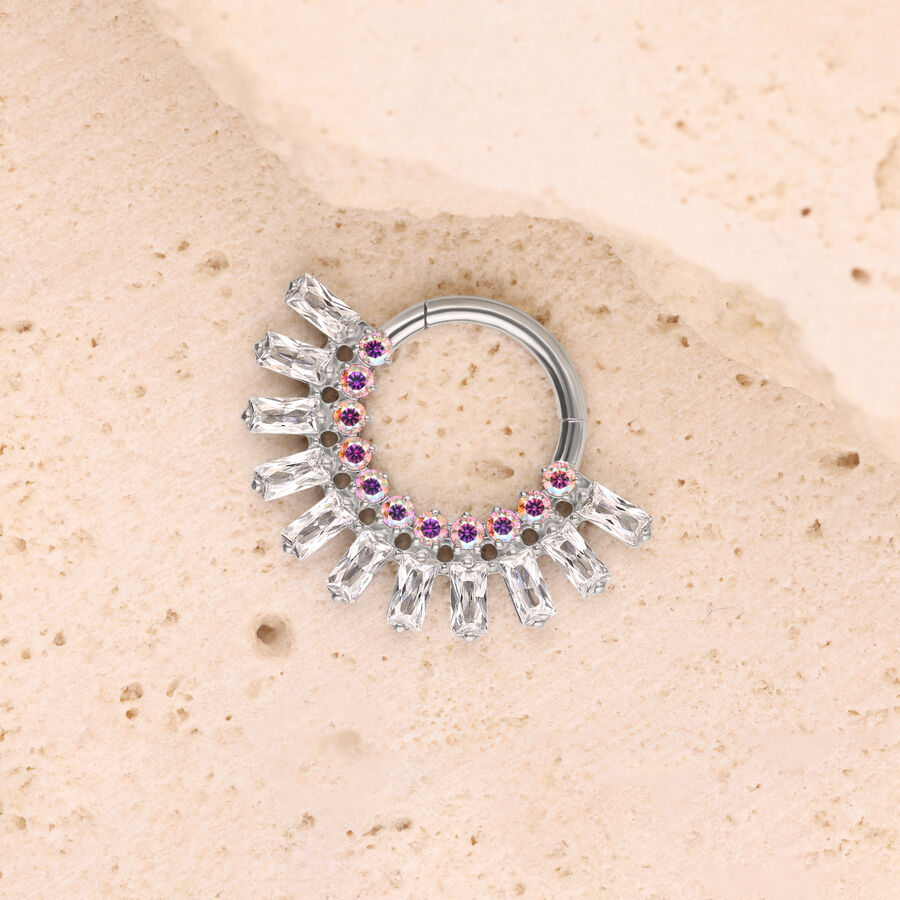 Anillo plateado con cristales claros y detalles rosados sobre fondo beige