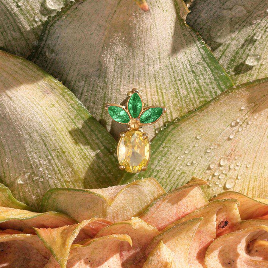 Accesorio de piercing de piña dorada con tres hojas verdes sobre cáscara de piña