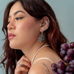 Mujer con varios piercings plateados en la oreja, lleva un collar de perlas y sostiene uvas.