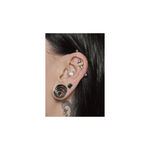 Lähikuva korvasta, jossa hopeinen industrial-piercing ja muita korvakoruja