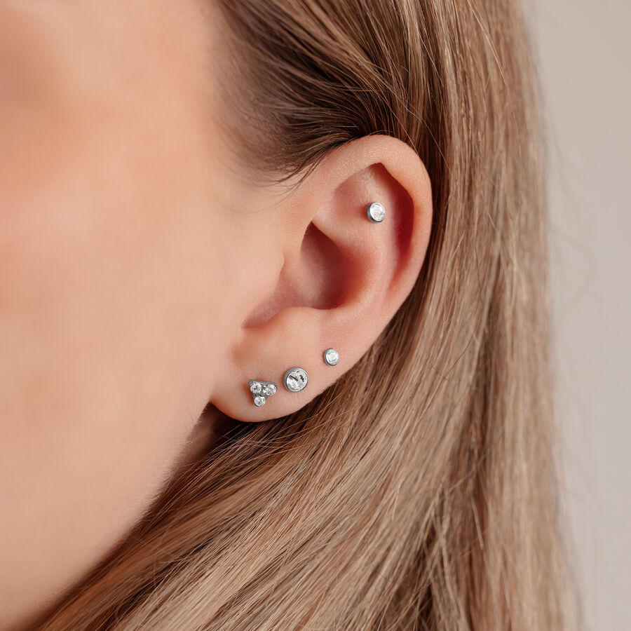 Primer plano de una oreja con disco plateado para triple piercing de 4,0 mm sobre fondo claro