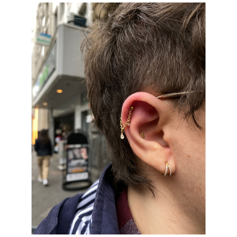 Anillo de piercing dorado con cristales en la oreja en un entorno urbano
