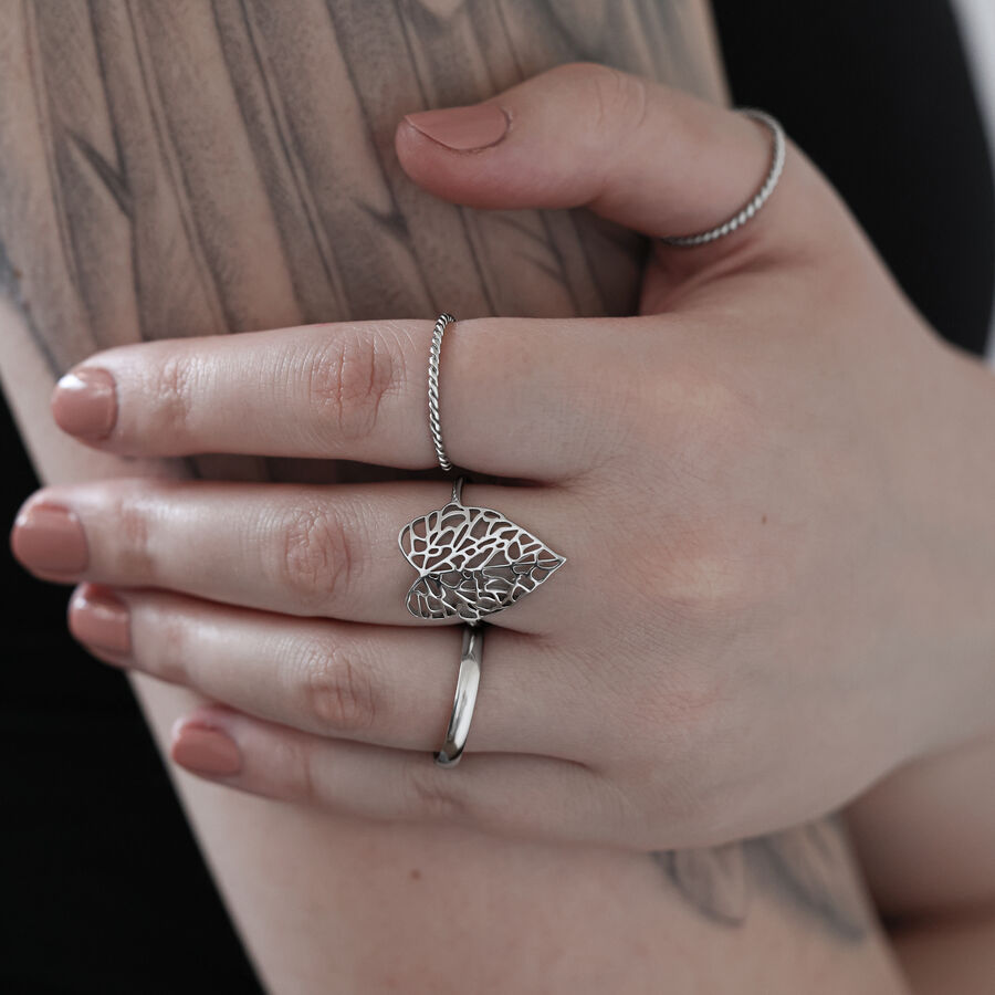 Anello a forma di foglia in argento su una mano tatuata davanti a uno sfondo chiaro