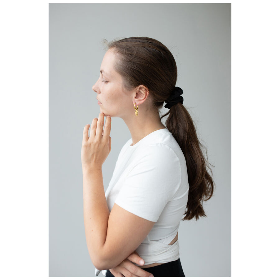 Donna con capelli lunghi indossa orecchini Hoops dorati su sfondo grigio