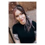 Frau mit schwarzen und silbernen Ohrringen und Piercings, lächelnd vor einer Steinwand