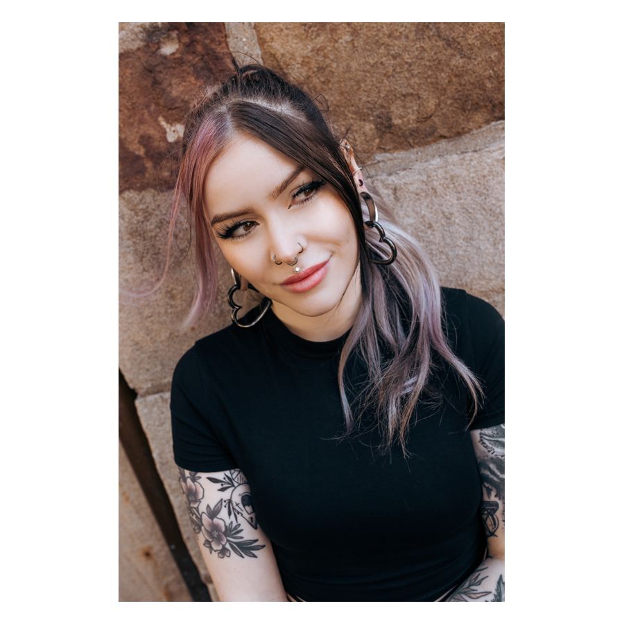 Frau mit schwarzen und silbernen Ohrringen und Piercings, lächelnd vor einer Steinwand
