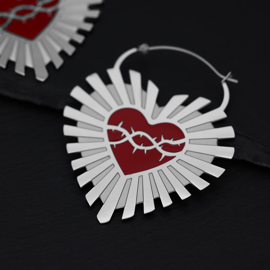 Aros plateados en forma de corazón con corona de espinas roja sobre fondo negro