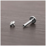 Cabezal de titanio plateado para piercing con cristal claro sobre madera oscura.