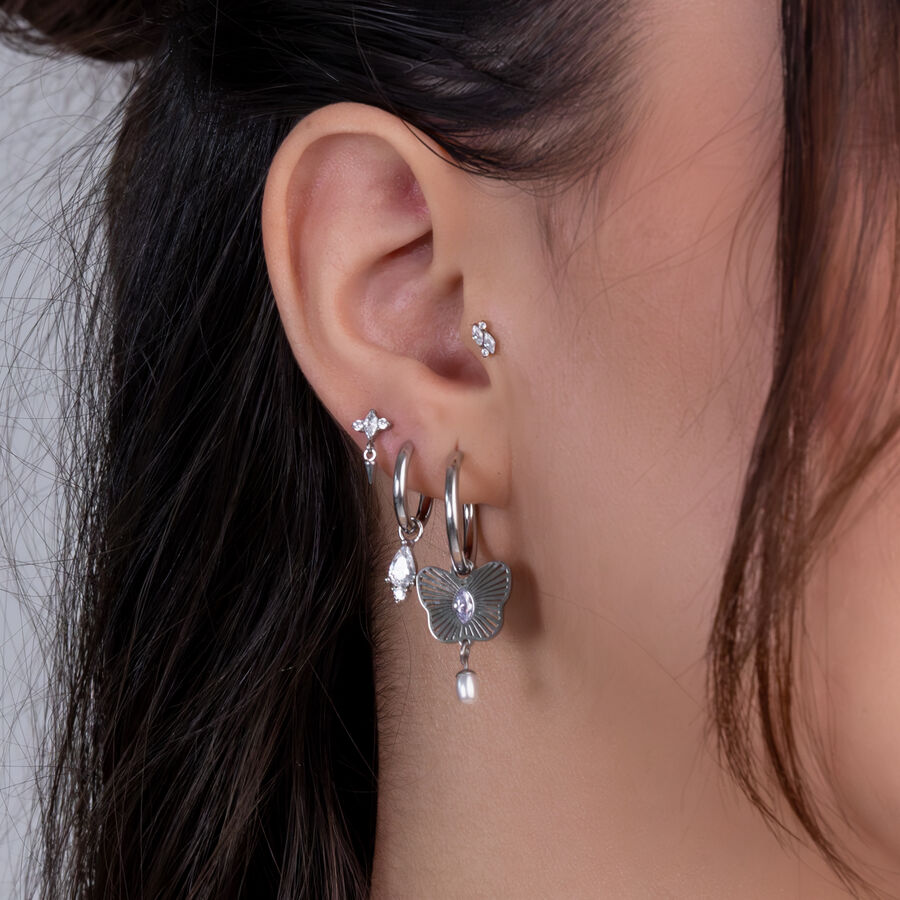 Primo piano di un orecchio con diversi piercing d'argento e cristalli chiari su sfondo chiaro