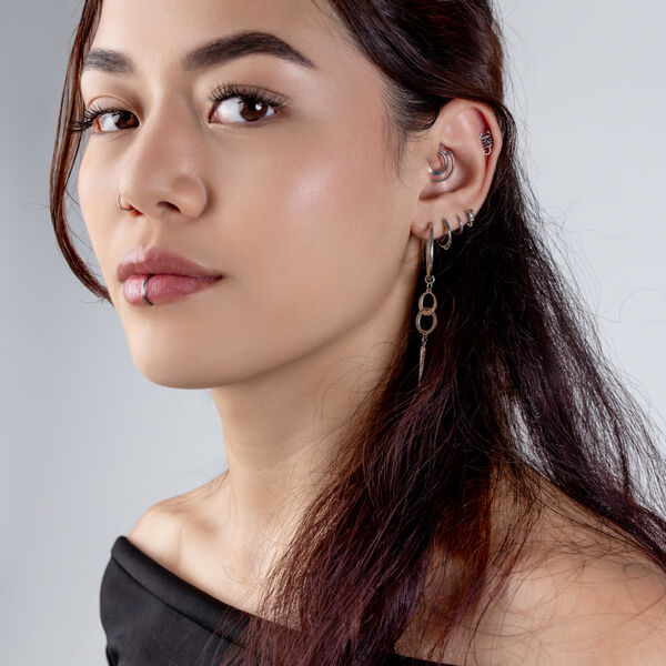 Mujer con un Clicker de doble anillo en la oreja y varios piercings, sobre un fondo gris