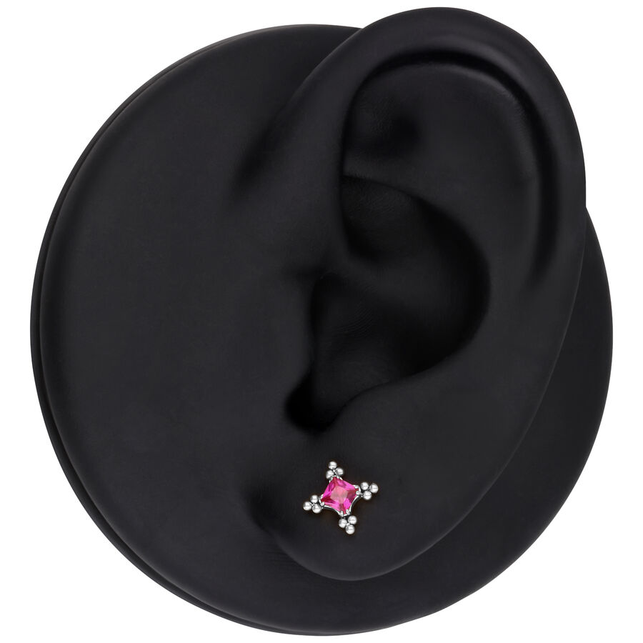 Modelo de oreja con accesorio de piercing plateado y cristal rojo sobre fondo negro