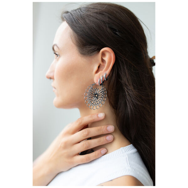 Mujer con pendientes Daisy Hoops de acero quirúrgico negro y plateado.