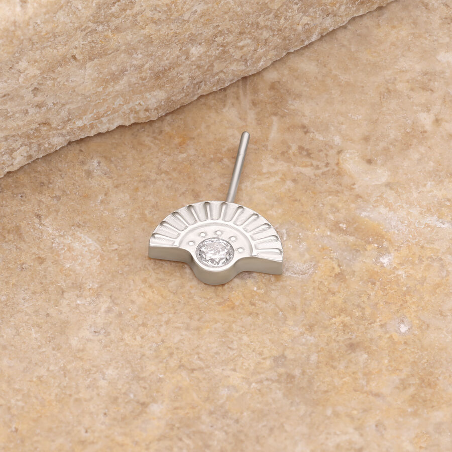 Piercing in oro bianco con pietra cristallina su sfondo di pietra beige