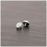 Accesorio de piercing plateado de titanio con cristal claro sobre superficie de madera