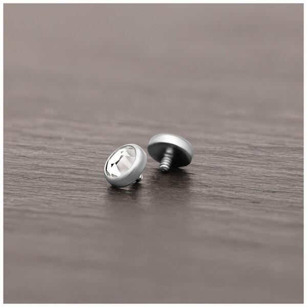 Accesorio de piercing plateado de titanio con cristal claro sobre superficie de madera