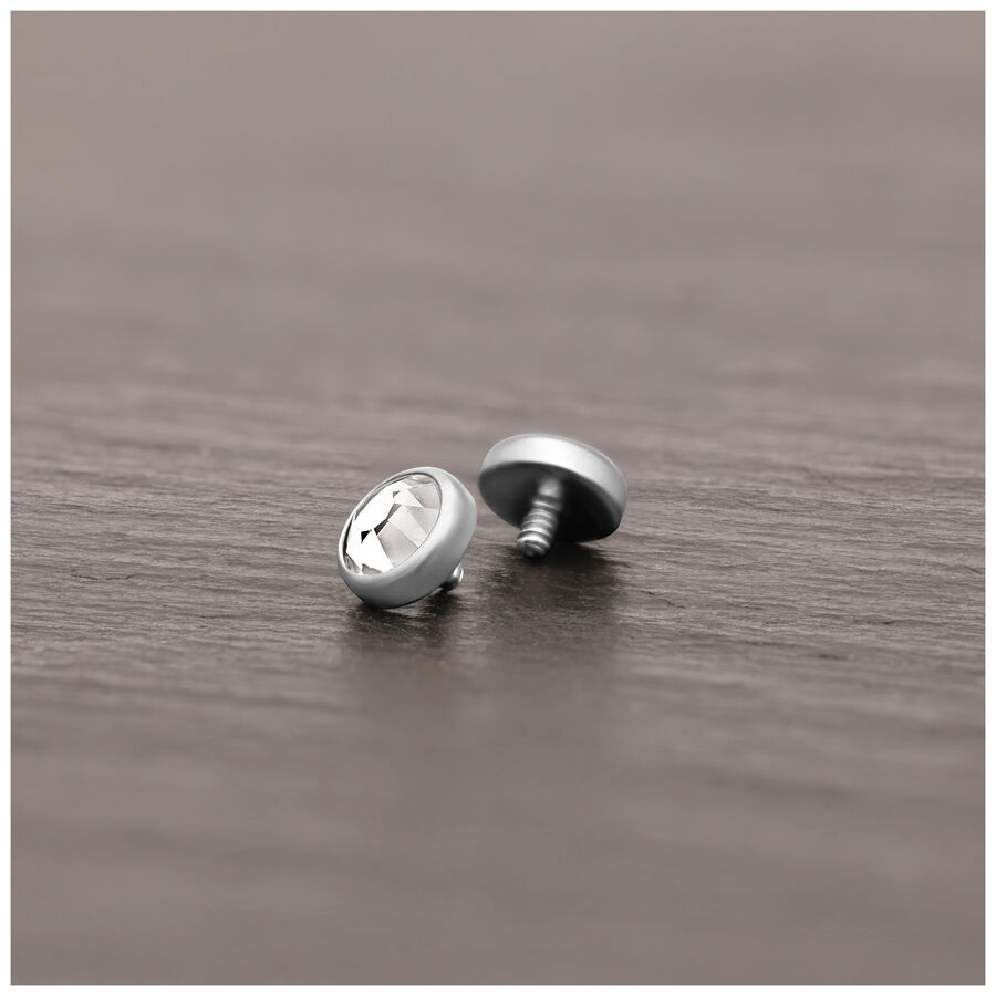 Accesorio de piercing plateado de titanio con cristal claro sobre superficie de madera