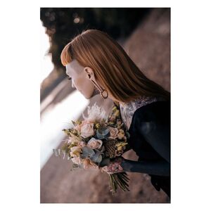 Person mit geflochtenen Ohrgewichten und Blumenstrauß am Seeufer