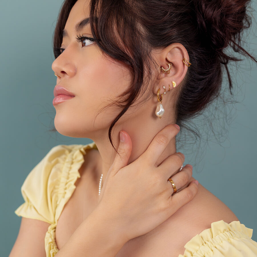 Mujer con pendientes y anillos dorados, camiseta amarilla, fondo azul