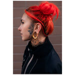 Donna con capelli rossi indossa Kaleidoscope Hoops in oro davanti a un muro di mattoni