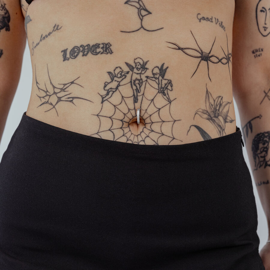 Bauchnabel Clicker aus schwarzem Titan mit klarem Kristall auf Haut mit Tattoos