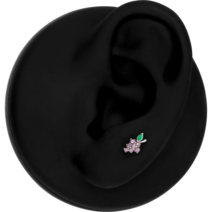 Accesorio de piercing plateado en forma de uva con piedras moradas y verdes en un modelo de oreja negra