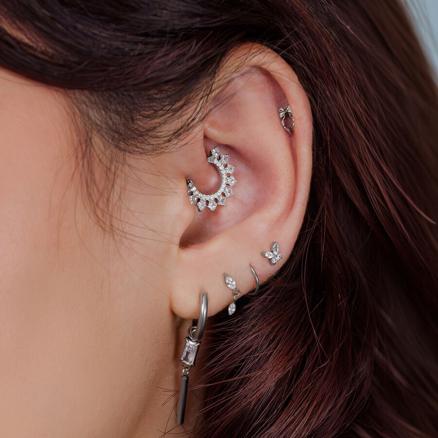 Primo piano di un orecchio con diversi accessori piercing argento e gioielli.