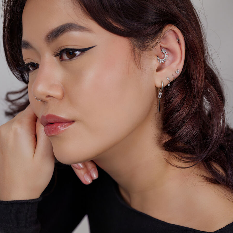 Donna con diversi piercing in argento, incluso un design a forma di luna sull'orecchio su sfondo chiaro