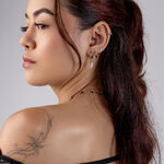 Donna con diversi piercing d'argento all'orecchio, capelli castani, tatuaggio sulla spalla