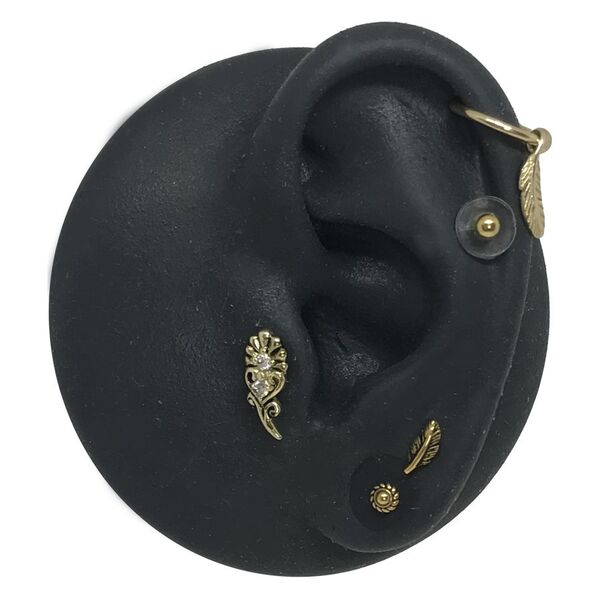 Modelo de oreja de silicona negra con apliques dorados para piercing sobre fondo blanco