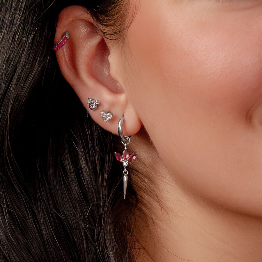 Primer plano de una oreja con varios pendientes de plata y cristales rojos, cabello oscuro de fondo