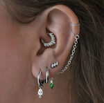 Mehrere Ohrringe im Ohr, darunter schwarze Little Tear Hoops mit grünem Kristall.