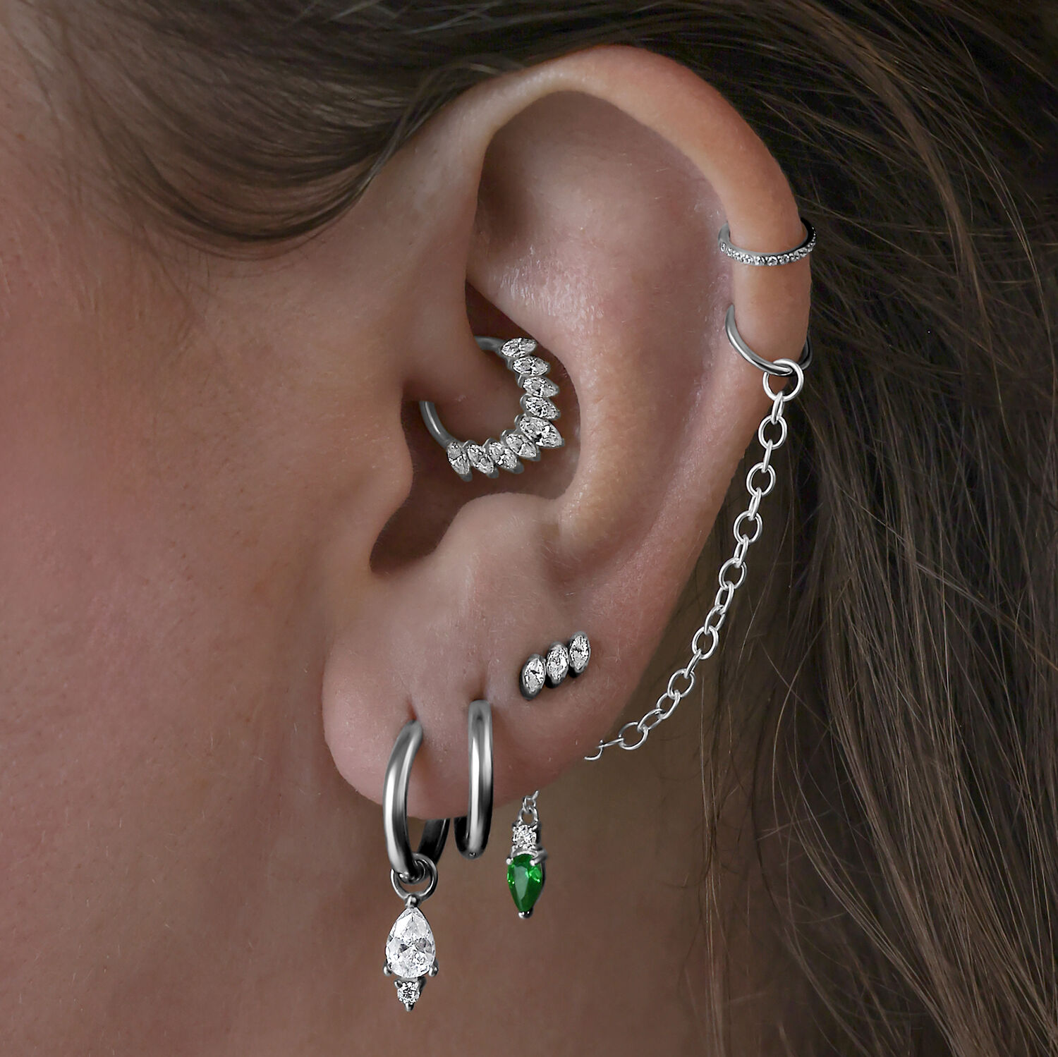 Little Tear Hoops in Schwarz und Smaragdgrün Mehrere Ohrringe im Ohr, darunter schwarze Little Tear Hoops mit grünem Kristall.
