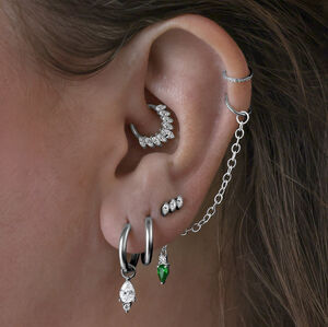 Little Tear Hoops in Schwarz und Smaragdgrün Mehrere Ohrringe im Ohr, darunter schwarze Little Tear Hoops mit grünem Kristall.