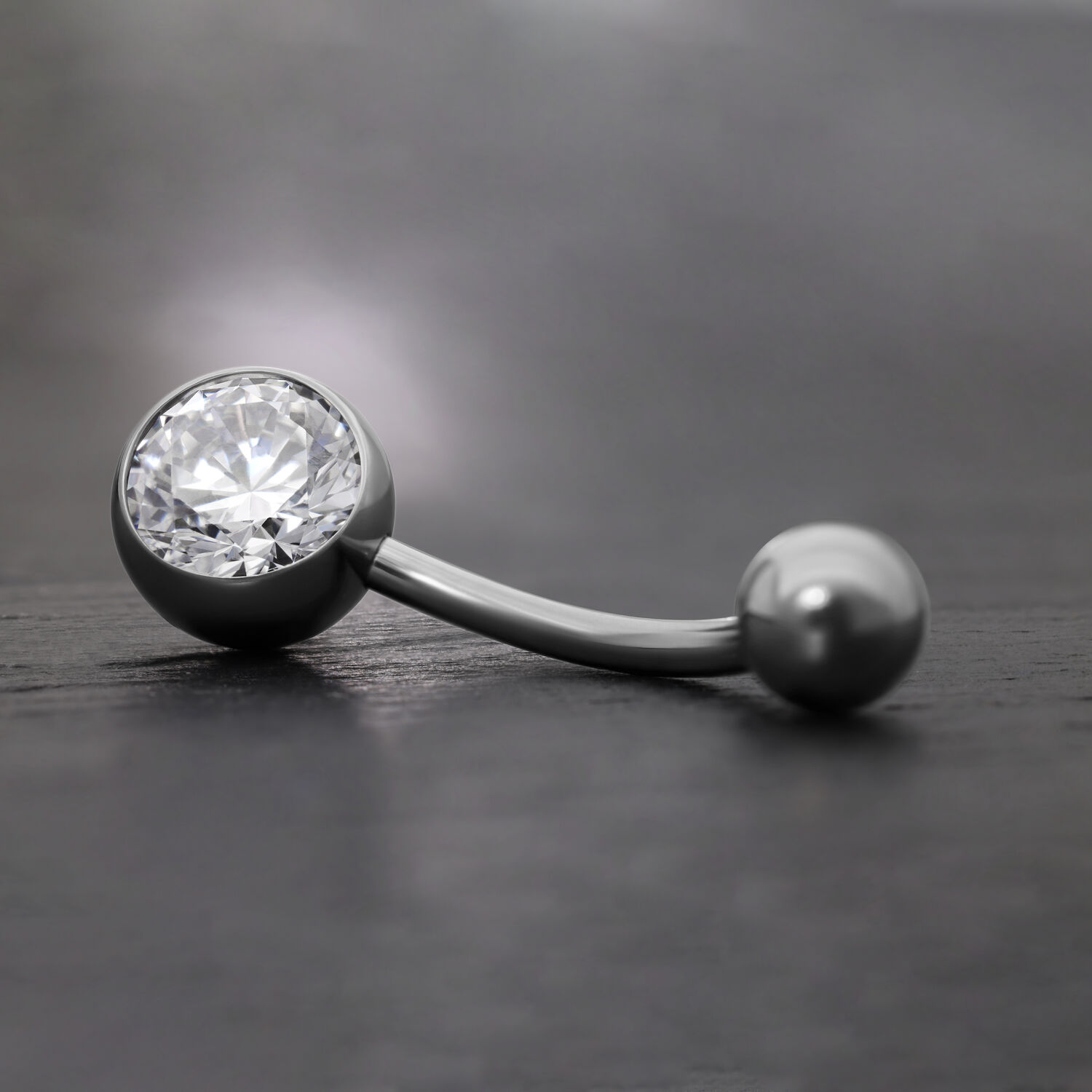 Elegantes Bauchnabelpiercing mit Kristall Schwarzes Bananabell aus Titan mit klarem Kristall auf grauem Hintergrund